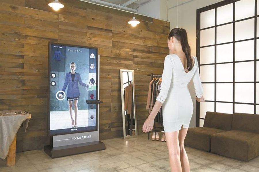 Shopper standing in front of a smart mirror kiosk, browsing outfit options on a touchscreen